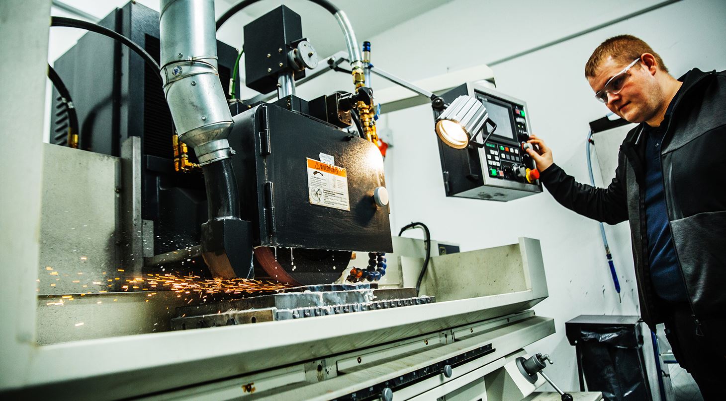 Mand betjener stor maskine til slibning af metalplatforme